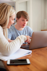 Downs Syndrome Man Sitting With Home Tutor Using Laptop For Lesson At Home