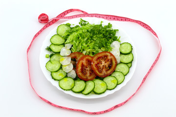 Sliced vegetables and greens in a white round plate: tomatoes, cucumbers, radishes, cabbage Beijing, dill, parsley, green onions. Around the pink measuring tape