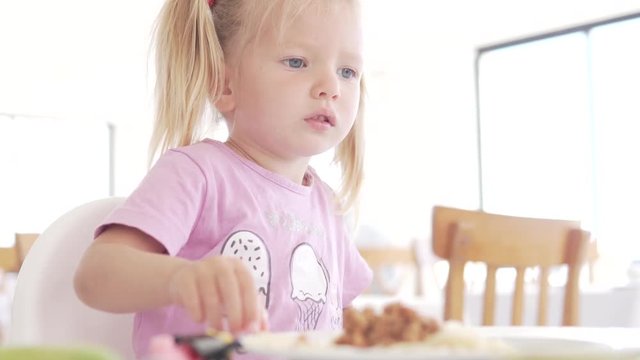 The little girl eats in the cafe. A child sits in a highchair in the dining room and eats french fries.