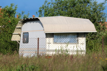 New white camper trailer parked in backyard and covered with protective nylon sheet surrounded with...