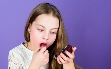 Lets get colorful. Little girl looking in glass and applying lip color. Small child painting lips with rosy color. Adorable makeup artist using color lipstick. Color festival, copy space