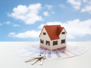 mortgage, real estate and property concept - close up of home model, money and house keys over blue sky and clouds background