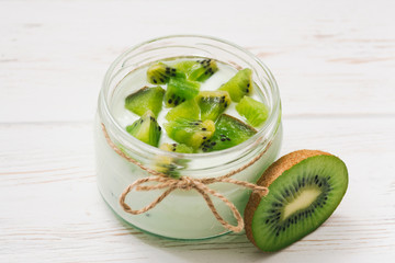 Yogurt with kiwi slices on a wooden white background.