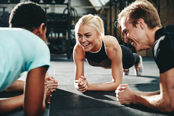 Smiling friends planking together during a gym workout session