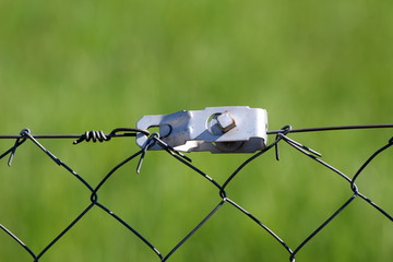 Wire fence strong grey metal tensioner closeup on light green background on warm sunny spring day