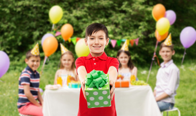 childhood and people concept - smiling little boy in red polo t-shirt with gift box at birthday party over friends in summer park background