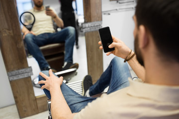 grooming, technology and people concept - man with smartphone at barbershop or hair salon