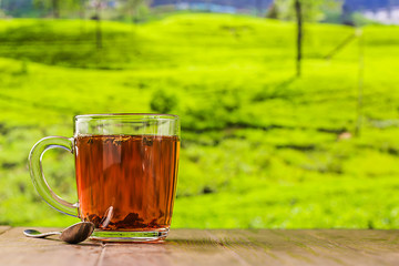 Tea in a glass cup on the wooden table and the tea plantations background