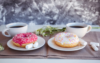 Glazed donut with black coffee and marshmallows. Pink and white tasty donuts on a table. Morning breakfast.