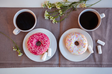 Glazed donut with black coffee and marshmallows. Pink and white tasty donuts on a table. Morning breakfast. Top view.