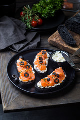 Healthy breakfast salmon sandwich with cream cheese and black bread on dark background, top view