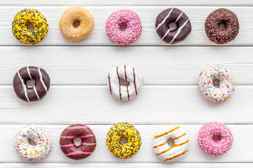 Traditional american donuts of different flavors on white wooden background flat lay pattern