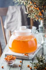 Vitaminic healthy sea buckthorn tea in a glass teapot with fresh raw sea buckthorn berries on a white wooden rustic background