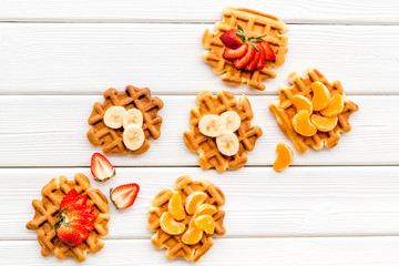 Breakfast with Belgian waffles with strawberry, tangerine and banana topings on white wooden background top view