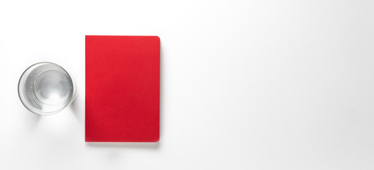red Notebook - notebad on white background isolated from above with a glass of water and space for...