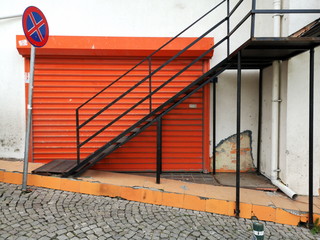 Treppenaufgang mit Geländer vor einem modernen Rolltor in leuchtendem Orange im strengen...