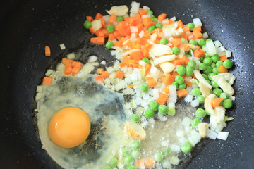 Small pieces of white onion, garlic, carrot, green peas and egg in boiled oil pan in process of fried rice cooking. Asian food ingredient.