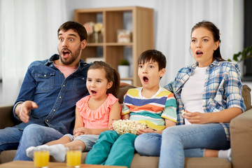 family, leisure and people concept - scared or surprised mother, father, son and daughter with popcorn watching horror on tv at home