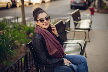 beautiful young girl in a leather jacket and scarf sitting on the streets of Chicago in the beautiful weather with phone