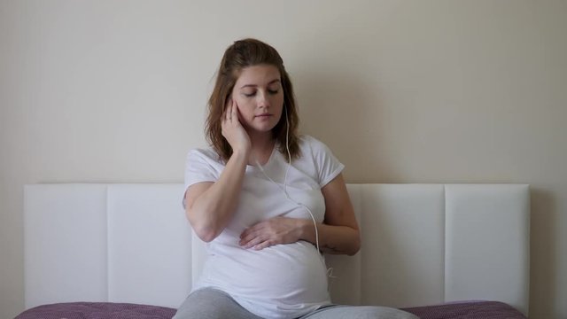 pregnant woman in a white t-shirt sitting on the bed at home
