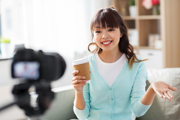 blogging, technology, videoblog and people concept - nice asian woman or blogger with camera and takeaway coffee cup recording video blog at home in morning