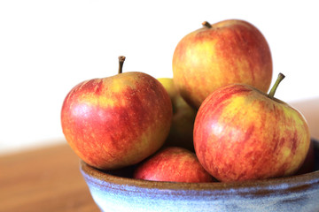 Composition with Yellow Red Apples in ceramic bowl on wooden and white background.