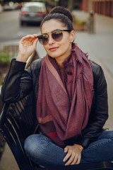 beautiful young girl in a leather jacket and scarf sitting on the streets of Chicago in the...