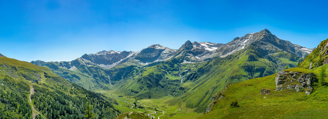 Naklejka na ściany i meble Panorama einer Bergkette mit saftigen Wiesen und massiven Felsen im idyllischen Salzburger Land unter blauem Himmel.