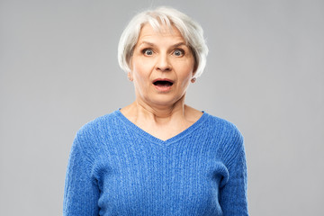 emotion, expression and old people concept - portrait of shocked senior woman in blue sweater with open mouth by hands over grey background