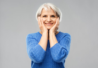 emotions and old people concept - portrait of amazed smiling senior woman in blue sweater over grey...
