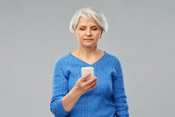 technology and old people concept - senior woman using smartphone over grey background