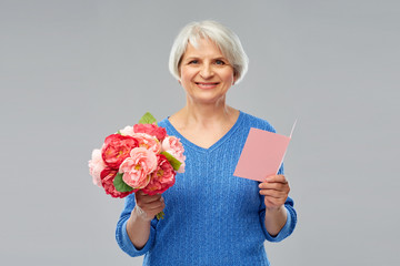 holidays, old age and people concept - happy smiling senior woman with flowers and greeting card...