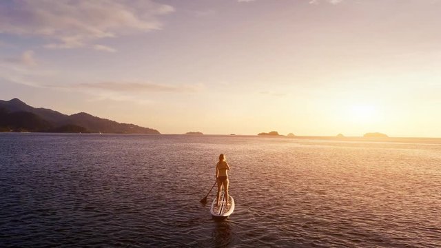 Girl stand up paddle boarding (SUP) on quiet sea at sunset, warm summer evening activity in nature, beach sport. 4K video