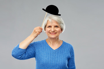 party props, photo booth and old people concept - portrait of smiling senior woman in blue sweater with black vintage bowler hat over grey background