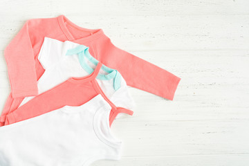 Baby bodysuit clothes over white wooden background. Copy space. Flat lay style