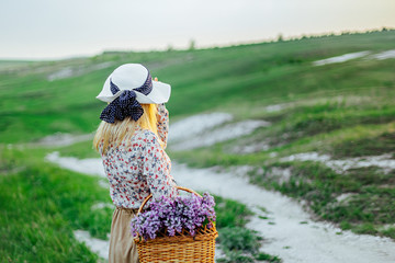 Young girl blonde in a hat and with a basket of flowers in a dress