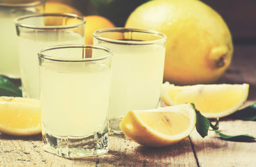 Lemon liqueur limoncello and fresh citrus on old wooden table, selective focus