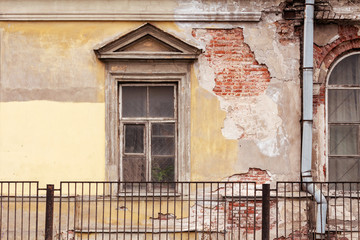 The wall of an old house with a window. fragment of the facade of an old building with cracks and crumbling plaster. facade of a dilapidated house with windows in the old style and brickwork
