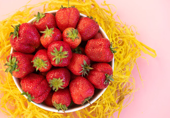 Fresh organic strawberry in the white bowl, on the pink background.