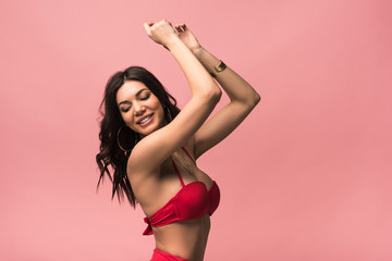 smiling attractive woman in swimsuit dancing isolated on pink