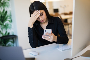 Portrait of tired woman talking phone near the computer at the office