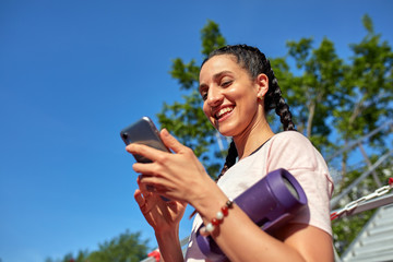 Young hipster girl is chatting via mobile phone in network with her friends and listening to music , pretty female is reading text message on her cell telephone while relaxing in the park