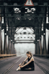 Ballerina is sitting and tying her pointe shoes between rails on the road.