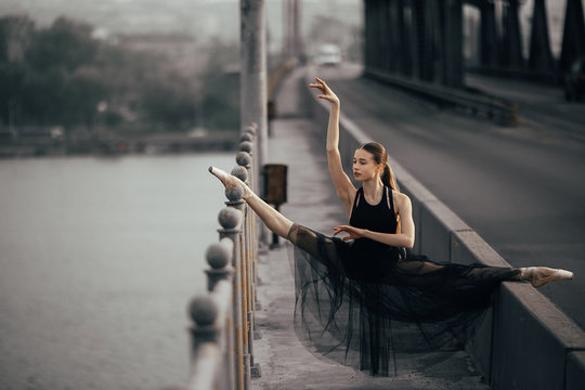 Ballerina sitting in twine pose on the bridge through the river.