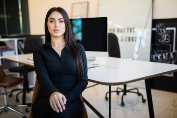 Portrait of a young businesswoman sitting at the table in office and looking at camera