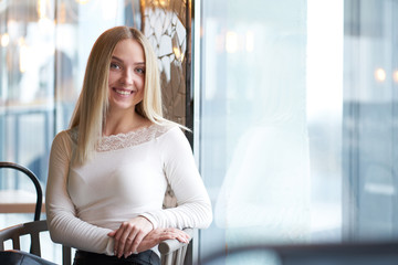 Portrait of young blonde smiling girl sitting near window