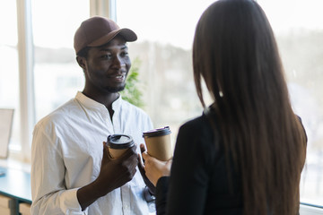 Smiling young mixed race colleagues in casual clothes have informal meeting while drinking coffee in modern office