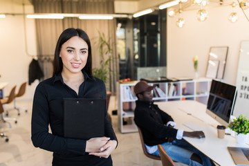Young cheerful woman having clipboard in hands in company office indoors