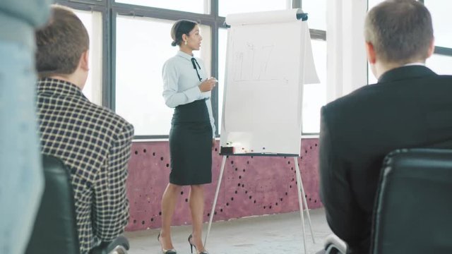 Young African American female manager holds a presentation near a flipchart and draws graphics. Coworking startup team