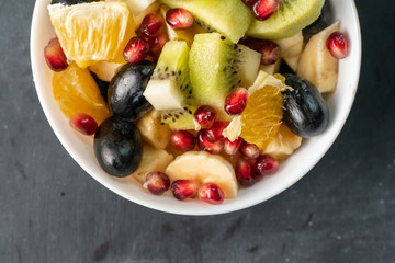 fruit salad with tropical exotic ripe fruits chopped in cubes, orange, kiwi, banana, grapes, pomegranates